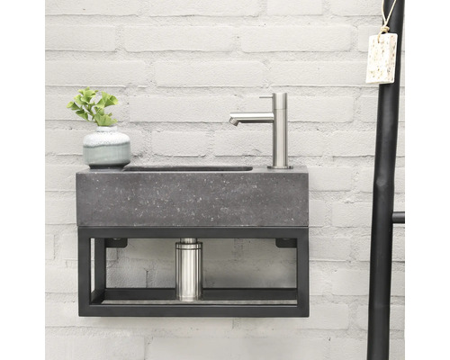 Moderne wastafel met grijze steenlook en zwart metalen frame aan een witte bakstenen muur