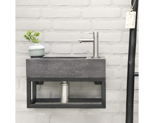 Wastafel met betonnen waskom en metalen frame tegen een bakstenen muur