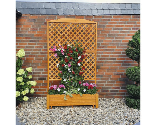 Houten plantenbak met klimrek en bloeiende planten voor een bakstenen muur