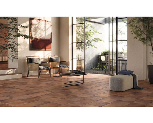 Lichte woonkamer met terracotta tegels, fauteuils en uitzicht op de tuin