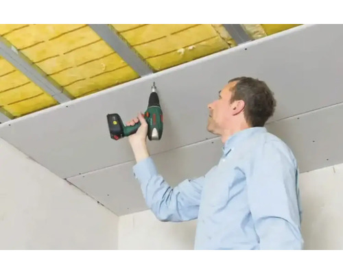 Een man bevestigt een gipsplaat aan een plafond met een boormachine.
