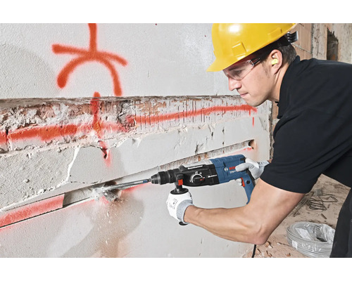 Man boort met een boorhamer in een muur. Hij draagt veiligheidsuitrusting.