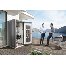 Scene met een tuinkast op een terras, waarin een barbecue en accessoires worden opgeborgen, en twee mensen