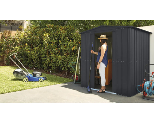 Tuinscene met grasmaaier en tuinhuisje waar een vrouw in staat