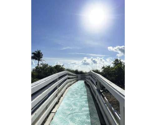 Houten loopbrug met patroon op weg naar het strand onder een blauwe hemel.