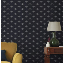 Woonkamer met behang met bijenpatroon, fauteuil en tafellamp.