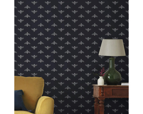 Woonkamer met behang met bijenpatroon, fauteuil en tafellamp.