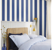 Slaapkamer met gestreept behang, rotan bed en blauw beddengoed