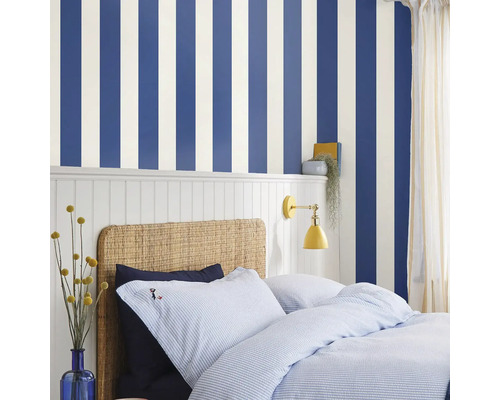 Slaapkamer met gestreept behang, rotan bed en blauw beddengoed