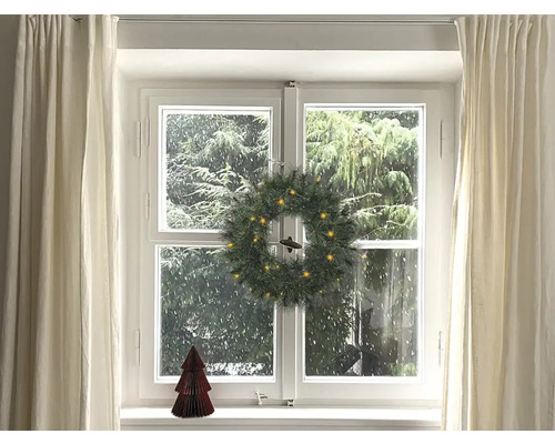 Gedecoreerd raam met kerstkrans, gordijnen en decoratieve boom.