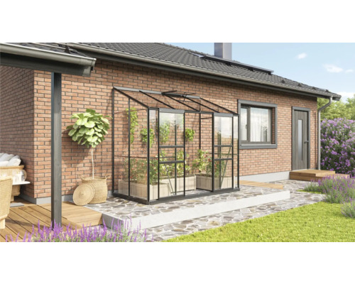 Kas met planten op een terras naast een woonhuis.