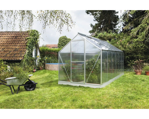 Kas in de tuin met planten en kruiwagen.