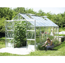 Kas met open ramen en planten, plus een vrouw die in de tuin werkt.