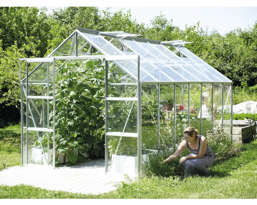 Kas met open ramen en planten, plus een vrouw die in de tuin werkt.