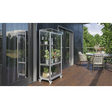 Een buitenscène met een plantenrek op wielen gevuld met diverse planten in potten, geplaatst op een terras naast een tafel met stoelen.