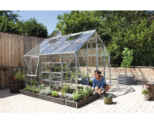 Kas met planten en een vrouw die in de tuin werkt.