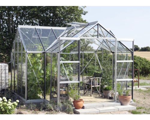 Kas met planten, stoel en potten in de tuin