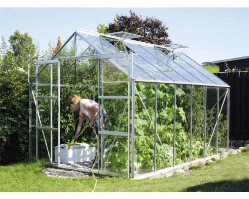 Kas in de tuin met vrouw die planten water geeft
