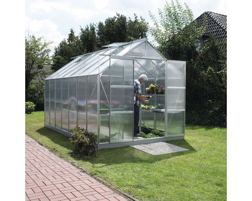 Kas met persoon, planten en rekken in de tuin.