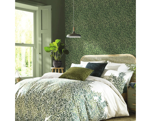 Slaapkamer met bed, nachtkastje, kamerplant en groen behang met bladerpatroon.