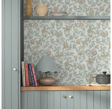 Scene met een plank gedecoreerd met serviesgoed en een lamp, voor een muur met een behang met vogel- en granaatappelmotief.