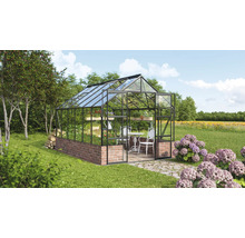 Kas met bakstenen fundering, glazen wanden en een tafel met stoelen erin in een tuin.