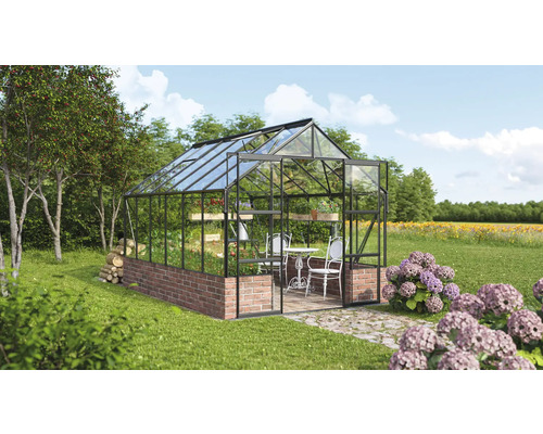 Kas met bakstenen fundering, glazen wanden en een tafel met stoelen erin in een tuin.