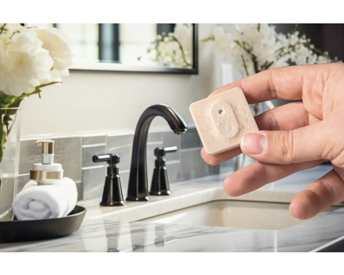 Scène van een badkamer met een handdoekenrek, een zeepdispenserfles, een wastafel en een hand die een vochtsensor vasthoudt.