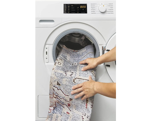 Een persoon plaatst een tapijt in een wasmachine.