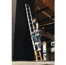 Man klimt op een telescopische ladder met een elektrisch gereedschap in zijn hand.