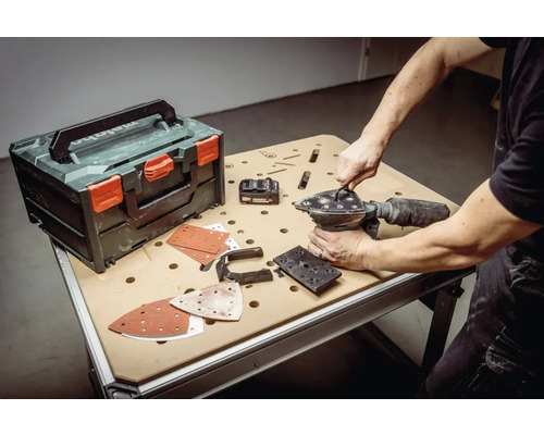Man verwisselt schuurpapier op een vlakschuurmachine naast een gereedschapskoffer op een werkbank.
