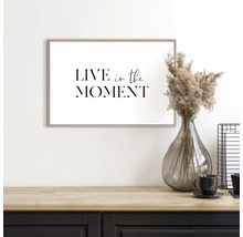 Decoratieve afbeelding met het opschrift ''Leef in het moment'' boven een tafel met vaas en kop.