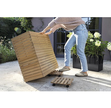 Een persoon verplaatst een houten plantenbak op een rolplank in de tuin.