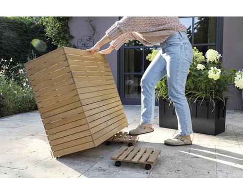 Een persoon verplaatst een houten plantenbak op een rolplank in de tuin.