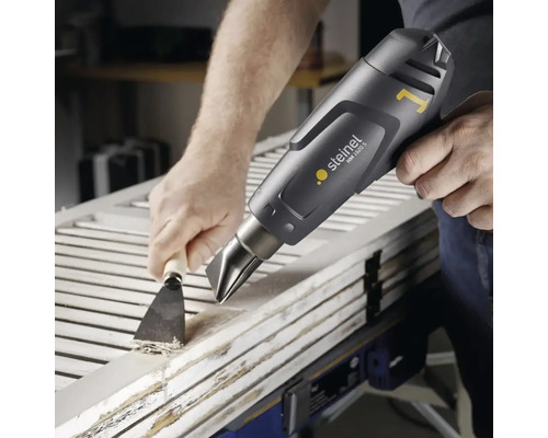 Vakman verwijdert verf van een houten deur met een heteluchtpistool en een plamuurmes