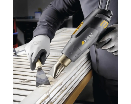 Een persoon verwijdert verf van een deur met een heteluchtpistool en een plamuurmes.