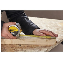 Een persoon meet een stuk hout met een Stanley PowerLock rolmaat van 10 meter.