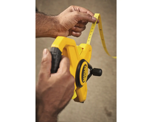 Een persoon houdt een gele rolbandmaat van 30 meter van het merk Stanley vast.