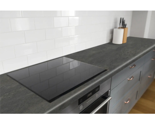 Keukenscène met inductiekookplaat, spoelbak en keukengerei op een werkblad.