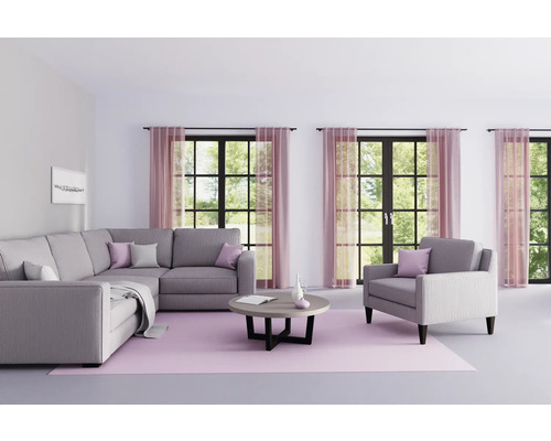 Woonkamer met grijze hoekbank, fauteuil, ronde tafel en roze vloerkleed voor ramen met gordijnen