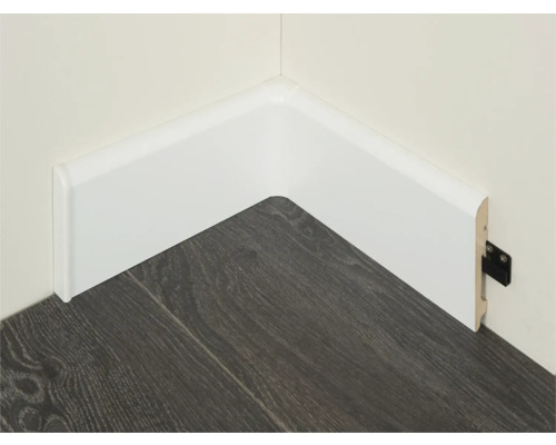 Witte kunststof plint op een muur met een donkere houten vloer