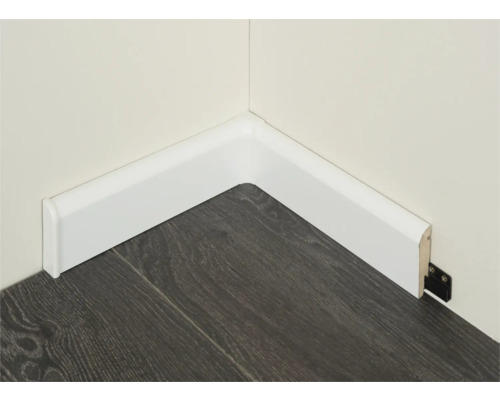 Hoek van de kamer met gemonteerde, witte plint op een donkere houten vloer