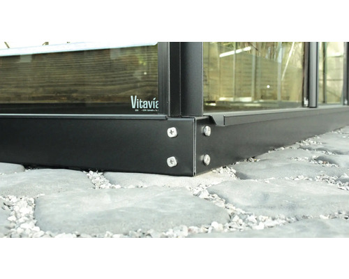 Detailopname van een Vitavia kas met metalen frame en schroeven op een stenen ondergrond