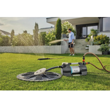 Scene met tuinwaterpomp, sproeier en persoon die de tuin besproeit op een gazon
