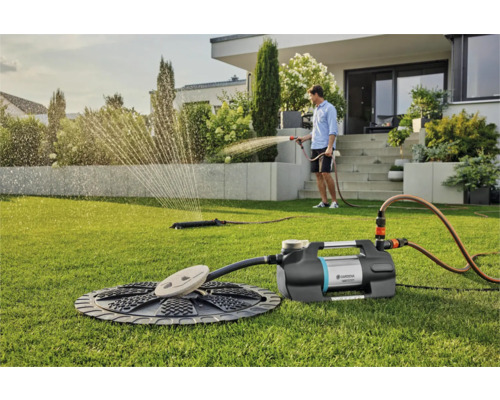 Scene met tuinwaterpomp, sproeier en persoon die de tuin besproeit op een gazon