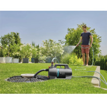 Tuin met sproeierpomp, waterreservoir en persoon met tuinslang