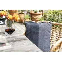 Scene met een wijnglas, een kussen op een rotan stoel en bloemen op een houten tafel in de buitenlucht.