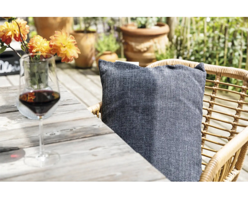 Scene met een wijnglas, een kussen op een rotan stoel en bloemen op een houten tafel in de buitenlucht.