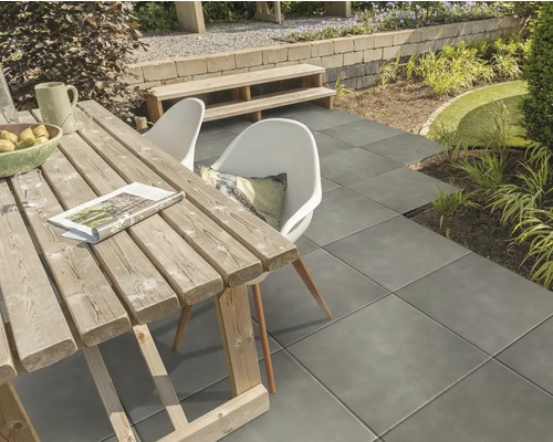 Buitenterras met terrastegels, houten tafel en tuinmeubelen