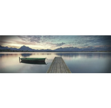 Een rustig meer met een houten steiger en een kleine boot op de voorgrond, met een berglandschap op de achtergrond.